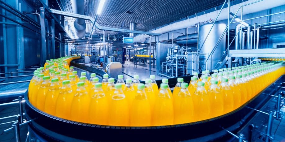 Máquina industrial de acero con filas de cilindros y botellas, números visibles en compartimentos, ruedas amarillas arriba Synergy Mechatronics.
